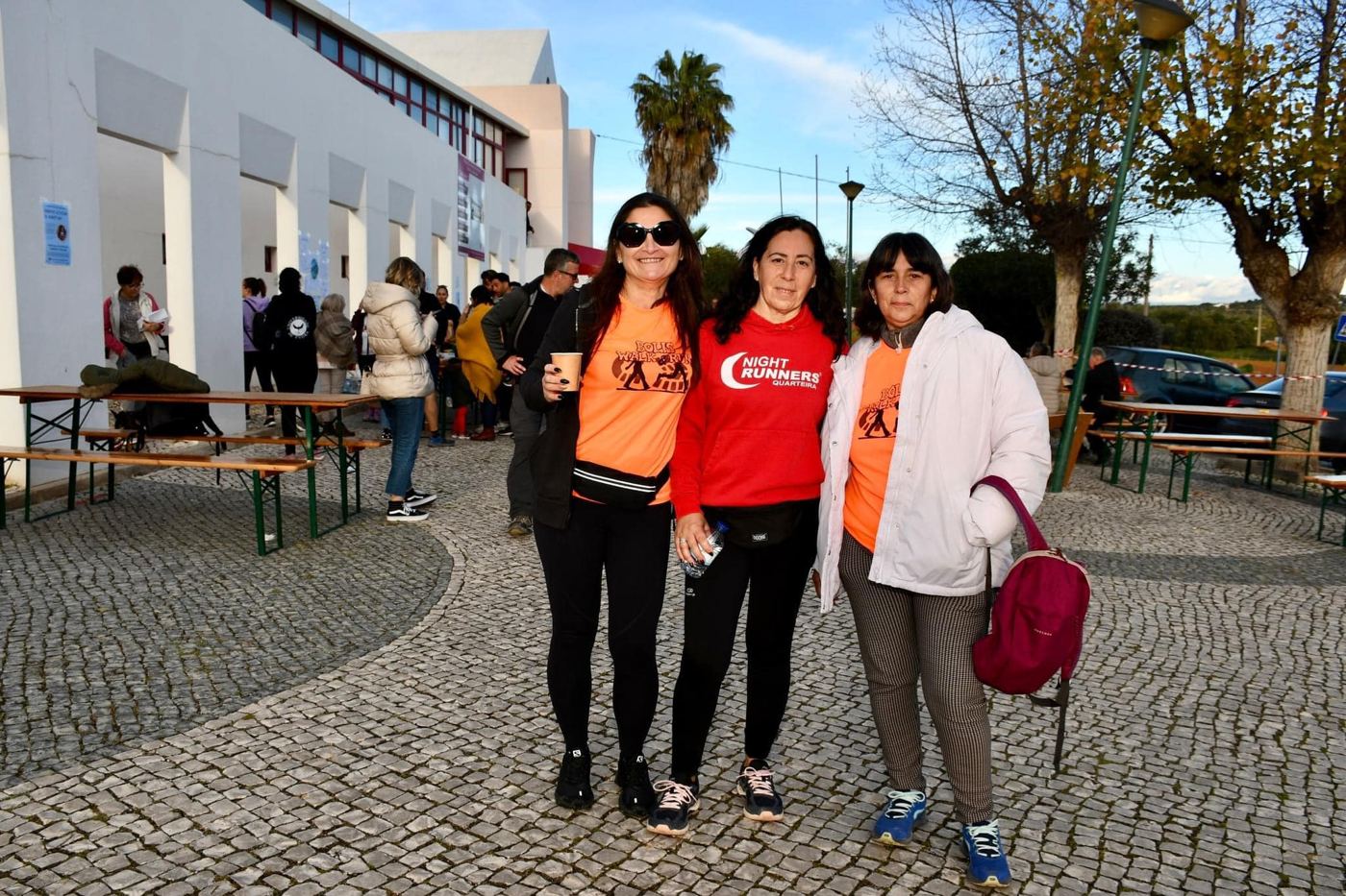 Três amigas de t-shirt laranja numa praça