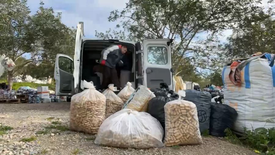 Uma carrinha aberta a descarregar sacos e garrafões de tampas entre árvores