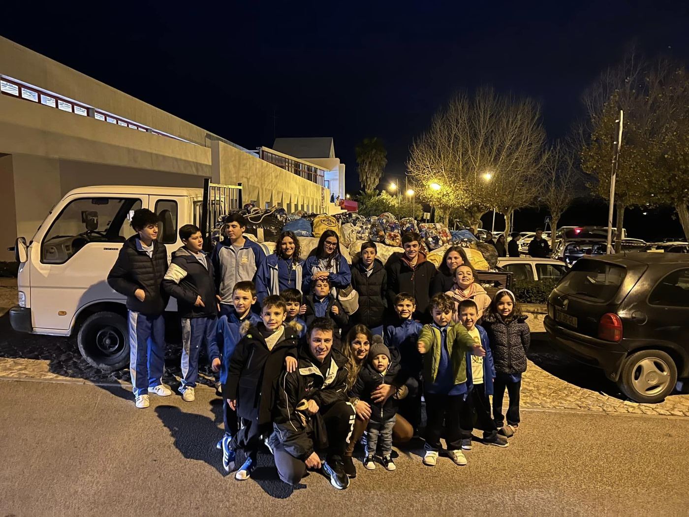 Um grande grupo reunido à noite junto a um camião